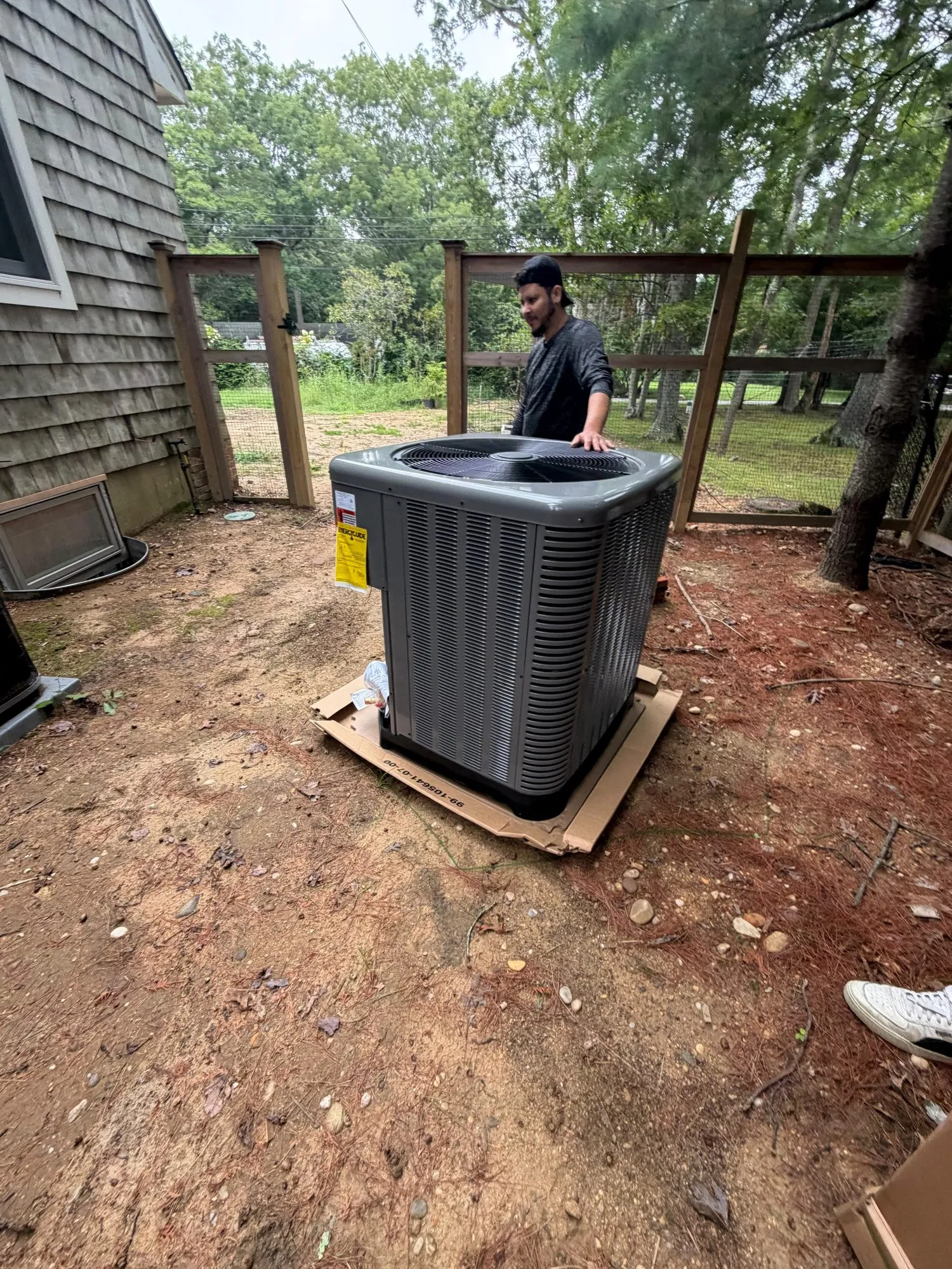 Technician setting a new central air conditioning condenser beside a shingled house