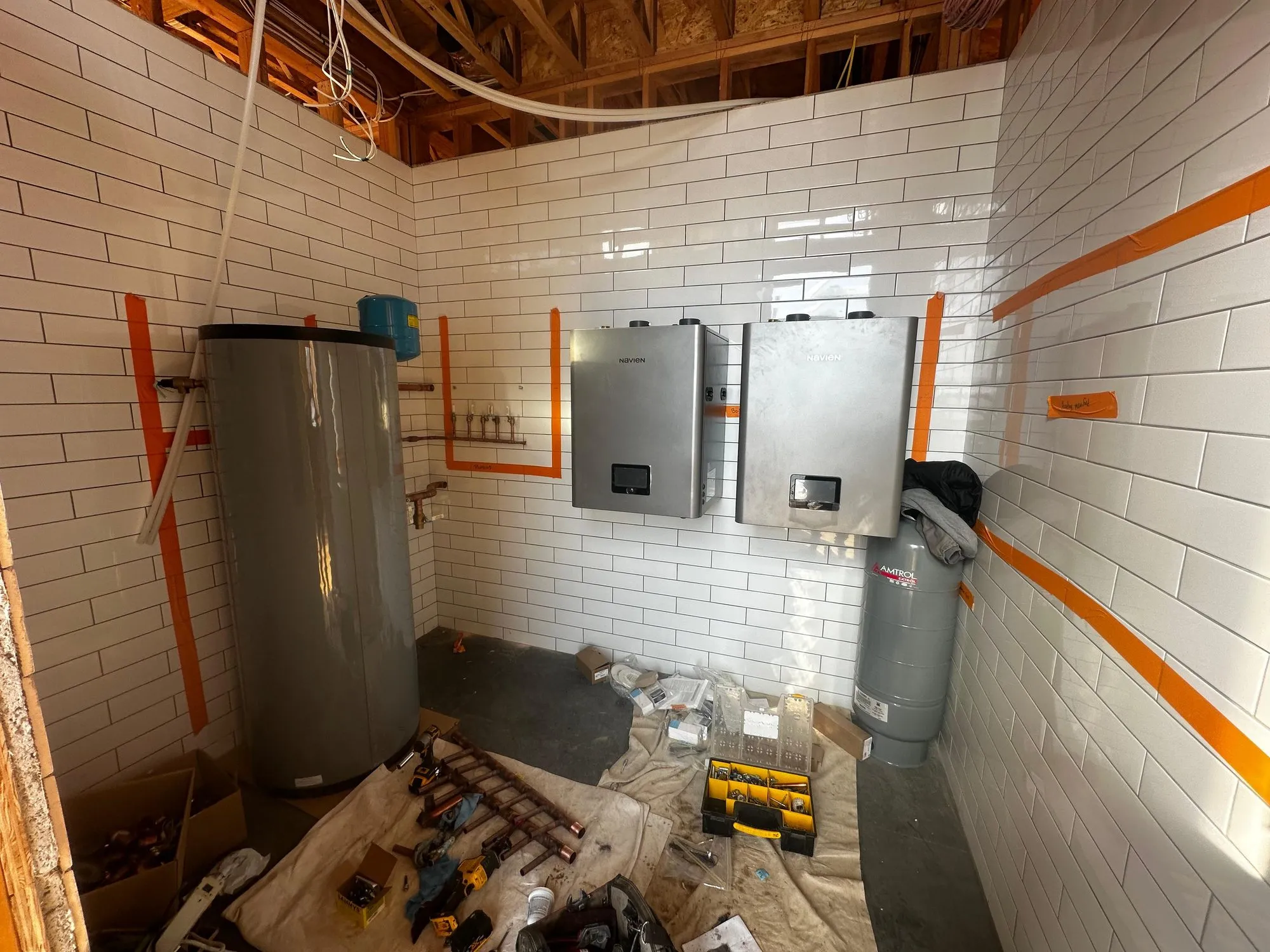 Two tankless water heaters and a storage tank being installed in a tiled mechanical room