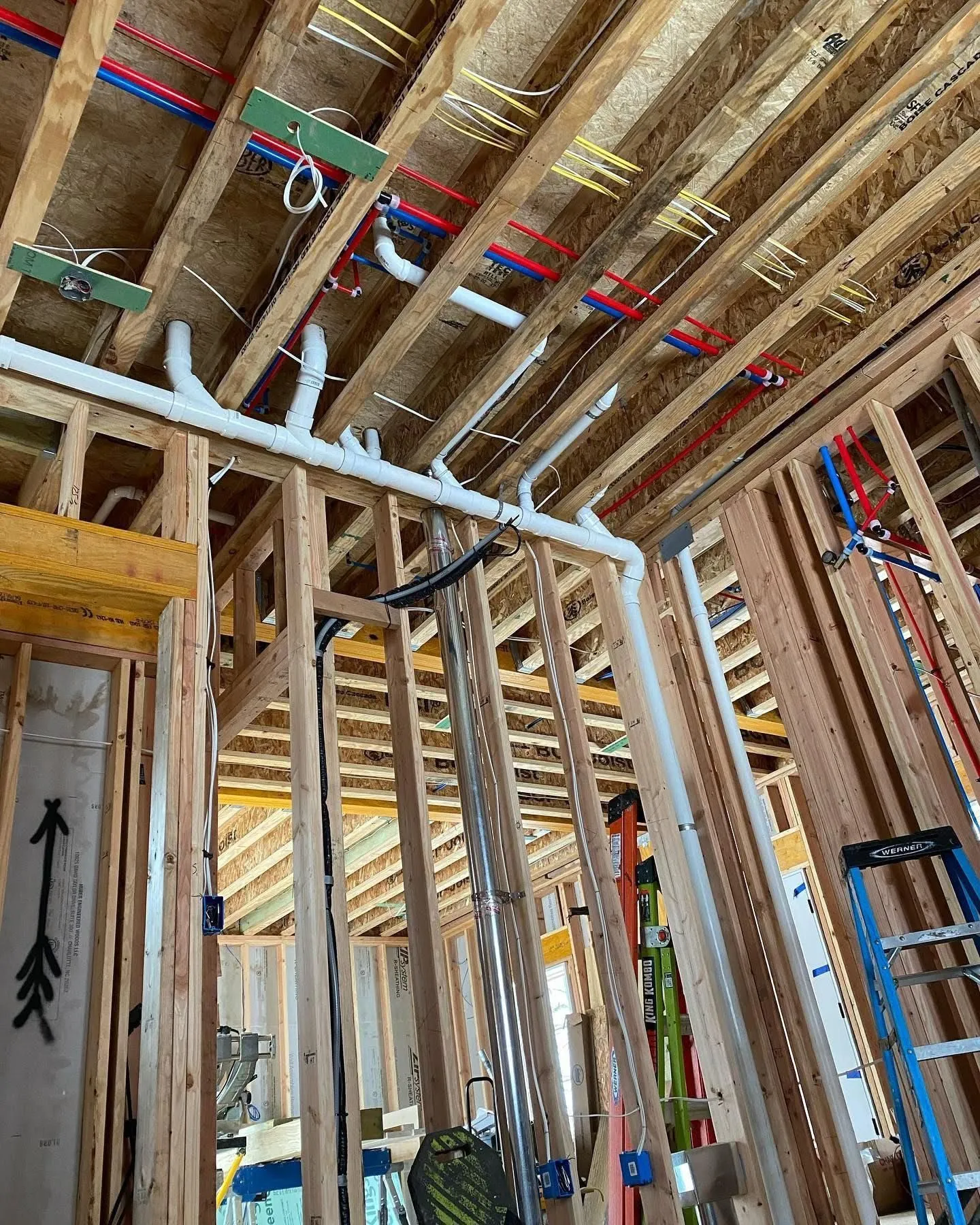 Overhead PEX and PVC rough-in plumbing run across open floor joists on a new build