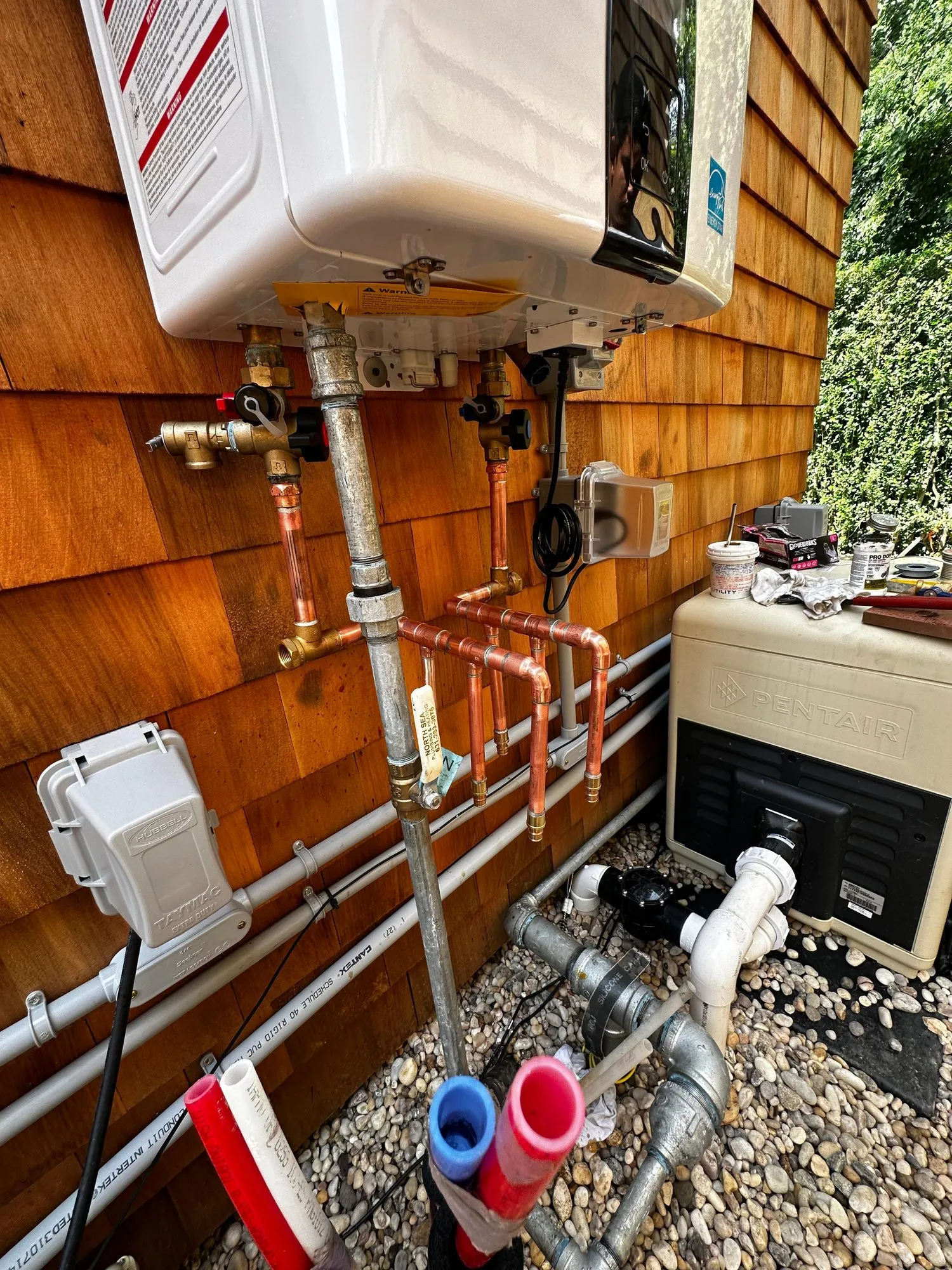 Exterior tankless water heater with new copper piping mounted on a cedar shingle wall