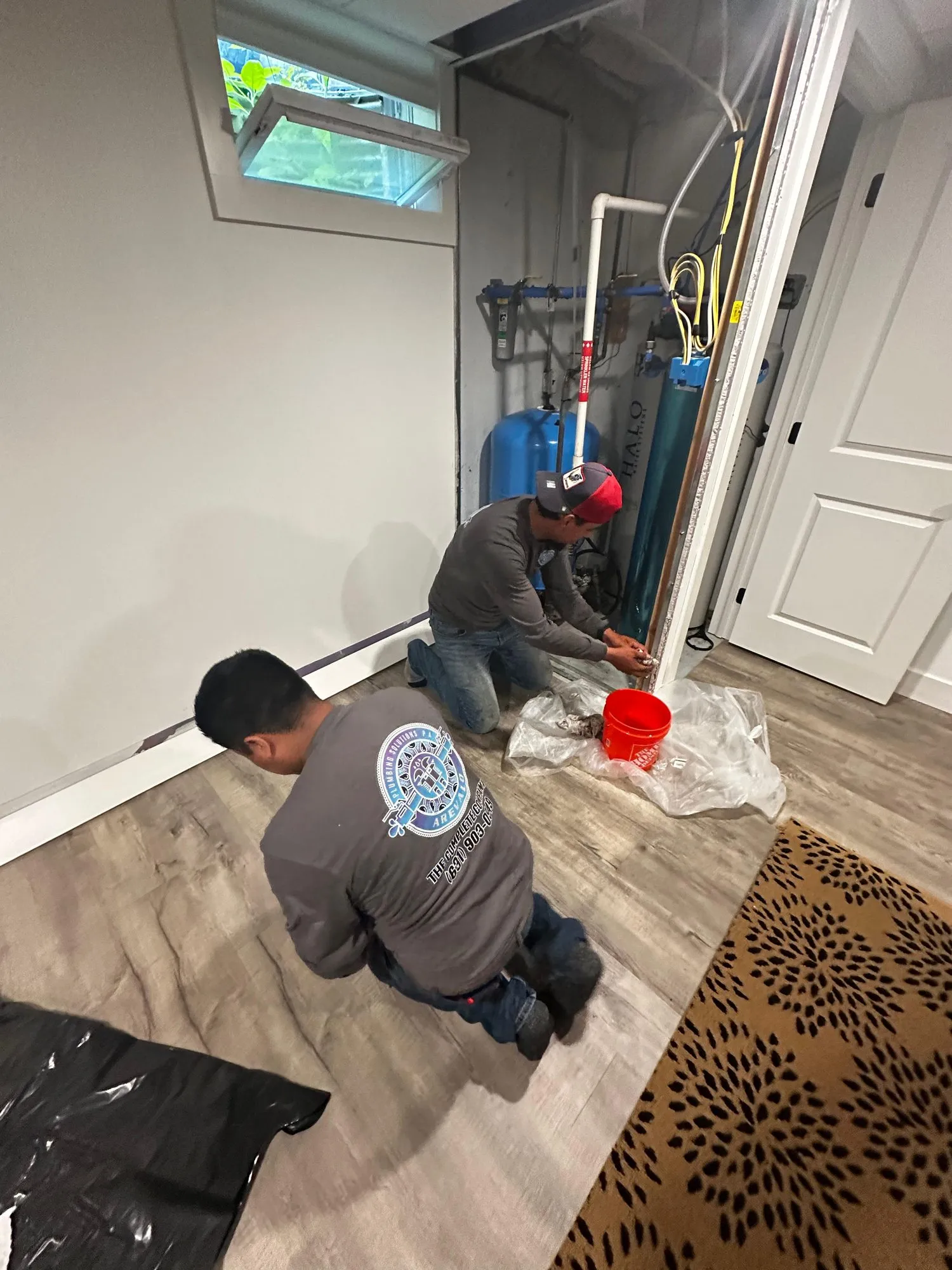 Two Plumbing Solutions P.A. technicians installing a water treatment system in a finished basement
